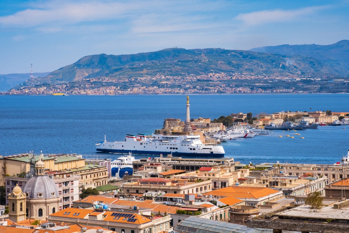 Blick über den Hafen von Messina mit der Statue der Madonna della Lettera, einer Fähre am Terminal und der kalabrischen Küste jenseits der Meerenge