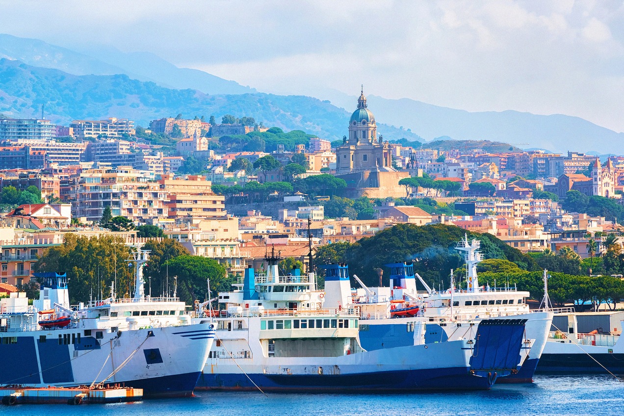 Passagierfähren im Hafen von Messina vor der Stadtsilhouette mit Kirchenkuppel und Hügeln